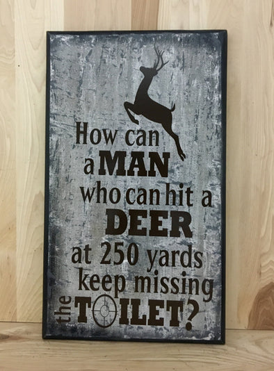 How can a man who can hit a deer at 250 yards keep missing the toilet? sign.